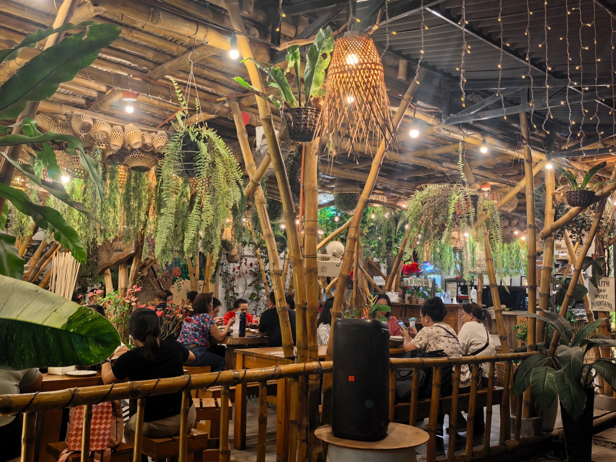 Guests at dining tables beneath hanging plants at D’ Garden at Calatao