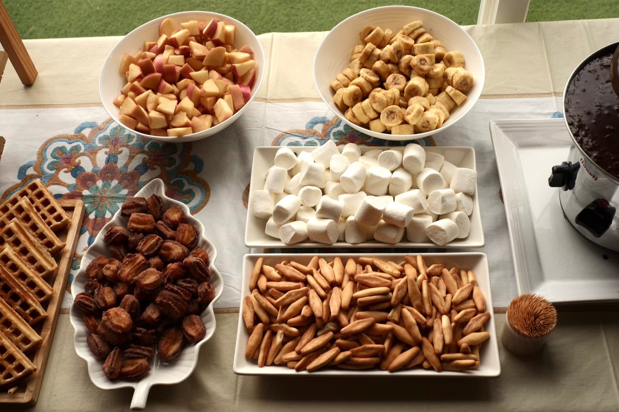 Fruit, marshmallows, waffles, and crackers arranged beside a chocolate fountain