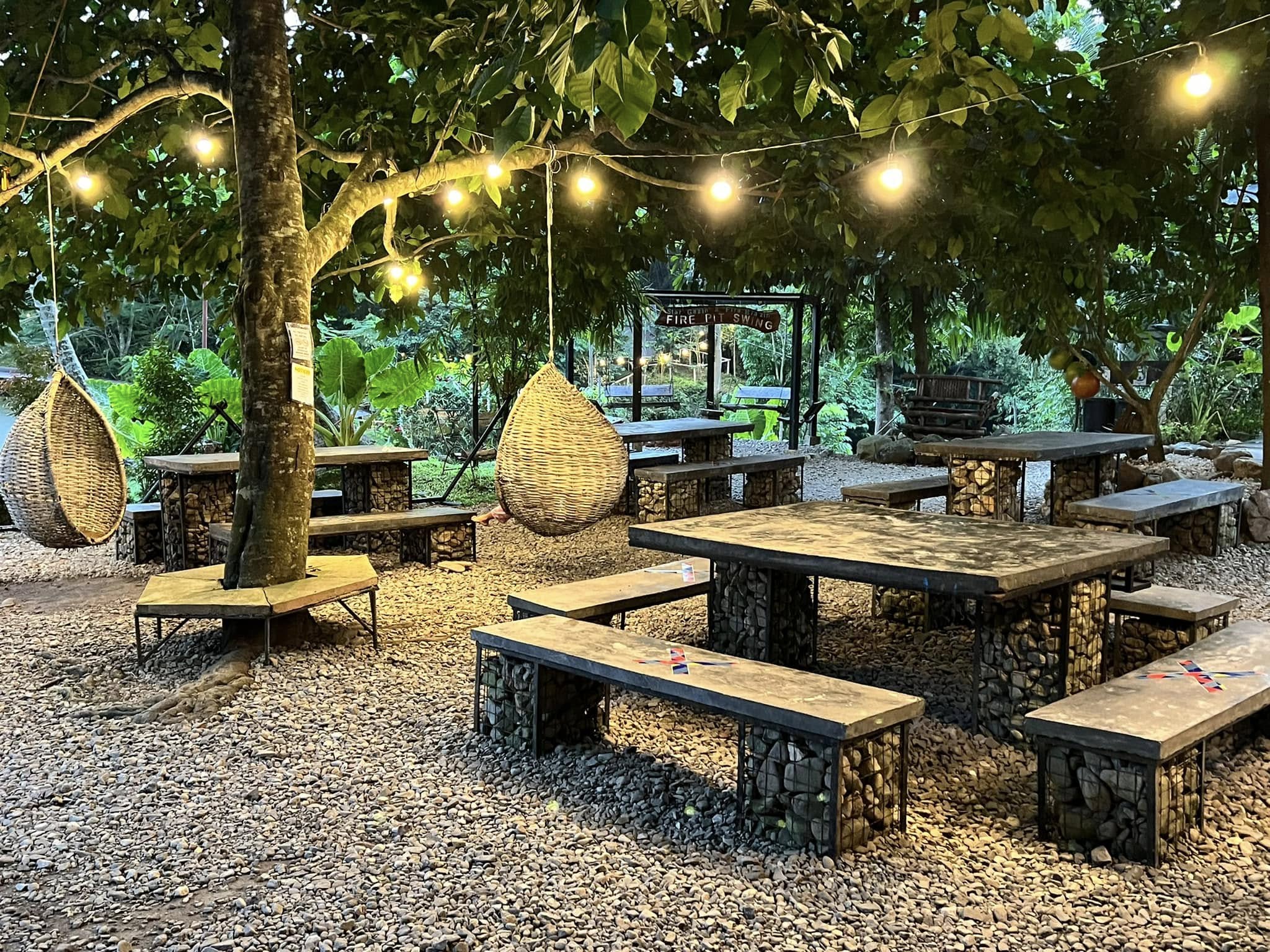 Garden tables and hanging chairs beneath trees and string lights