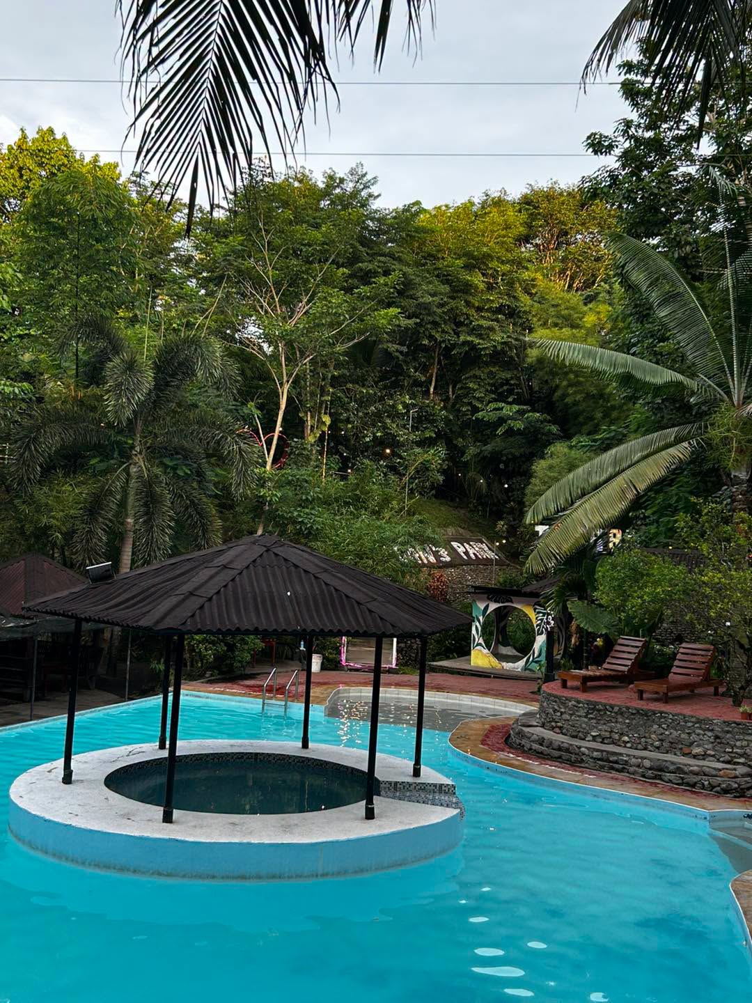 Central pool gazebo with tropical greenery behind it